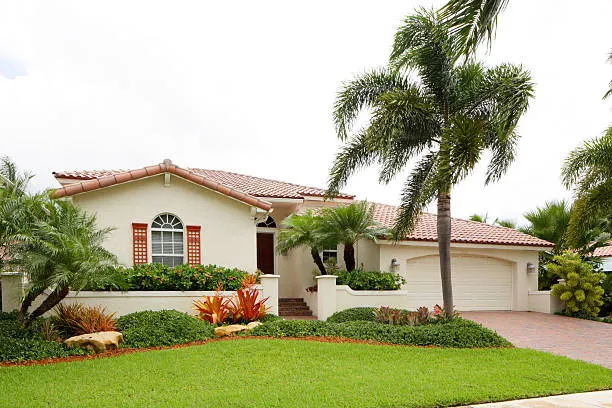 A well-maintained lawn in front of a beautiful Orlando home with lush greenery, palm trees, and vibrant landscaping, showcasing the results of professional lawn care services.