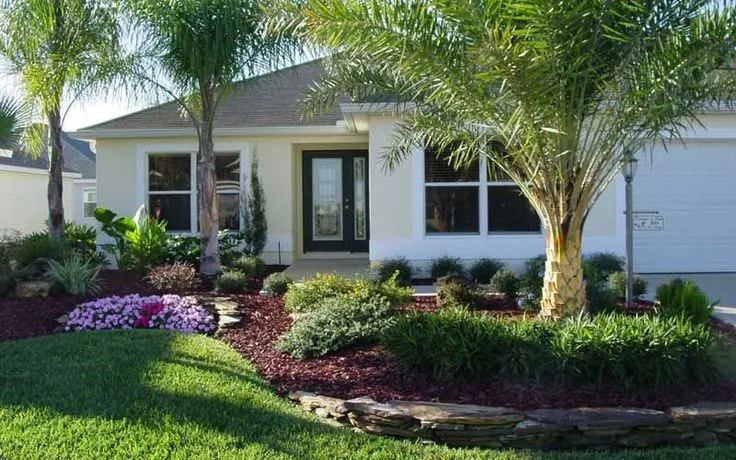 Well-maintained front yard of a house in St. Cloud with vibrant green grass, decorative plants, and palm trees, showcasing the results of professional lawn care services.