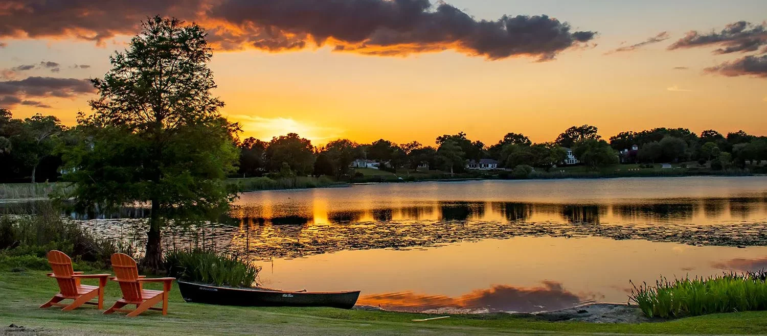 A stunning sunset over a tranquil lake in Maitland, with a canoe on the shore, illustrating the natural beauty and peaceful environment of the area.